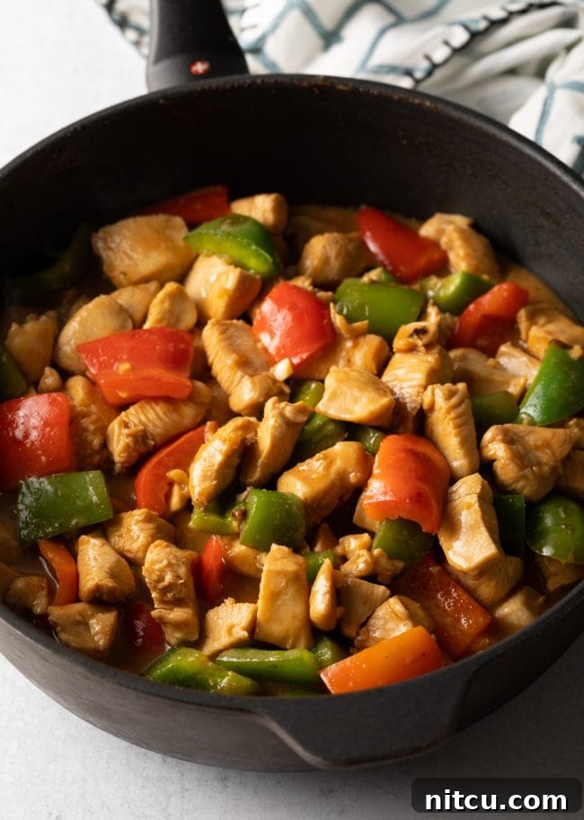 Cooked marinated chicken pieces with red and green bell peppers in a large skillet.