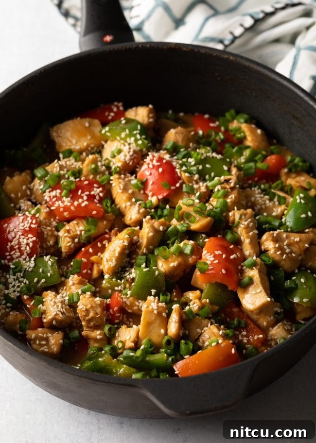 Top view finished skillet of cooked chicken and peppers, topped with sliced scallions and sesame seeds.