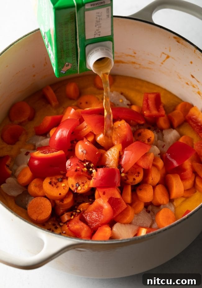 Authentic West African Maafe Peanut Stew 9 Chicken broth being poured over bell peppers, carrots, chicken, and the creamy Maafe base in a pot.