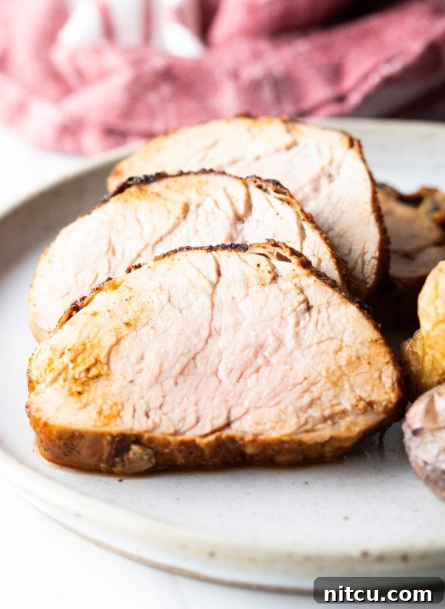 A close-up view of succulent slices of air-fried pork tenderloin on a white dinner plate, highlighting its juicy interior and flavorful crust.