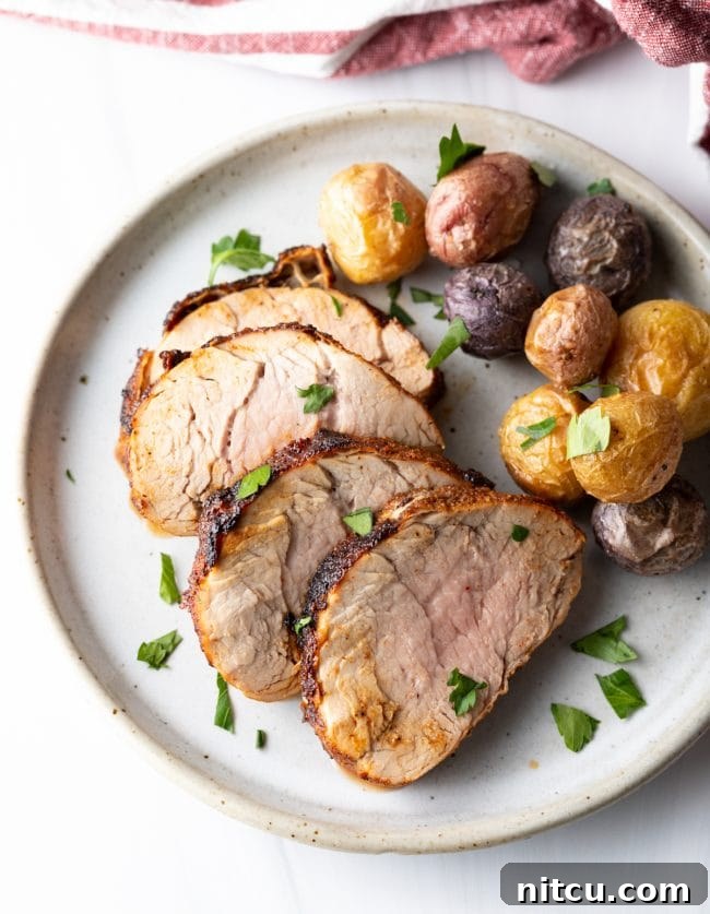 A top-down view of a dinner plate featuring four slices of perfectly cooked air-fried pork tenderloin alongside a side of golden baby potatoes.