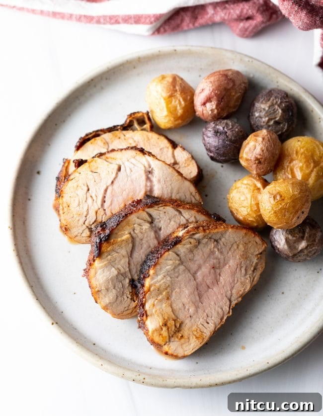 A beautifully presented dish featuring slices of perfectly cooked air-fried pork tenderloin alongside roasted baby potatoes, ready to be served.