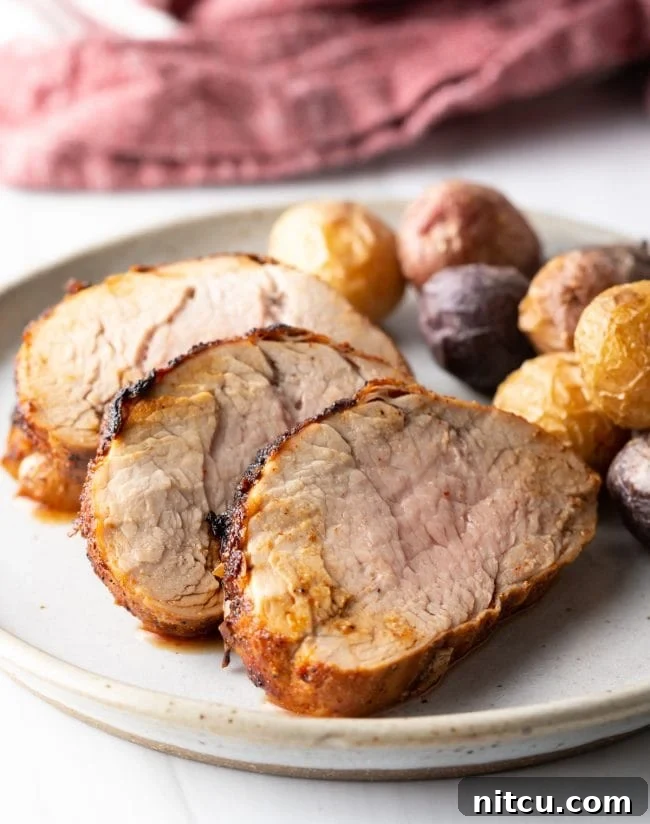 Close-up side view of perfectly sliced air-fried pork tenderloins arranged on a white plate, accompanied by small roasted potatoes for a complete meal.