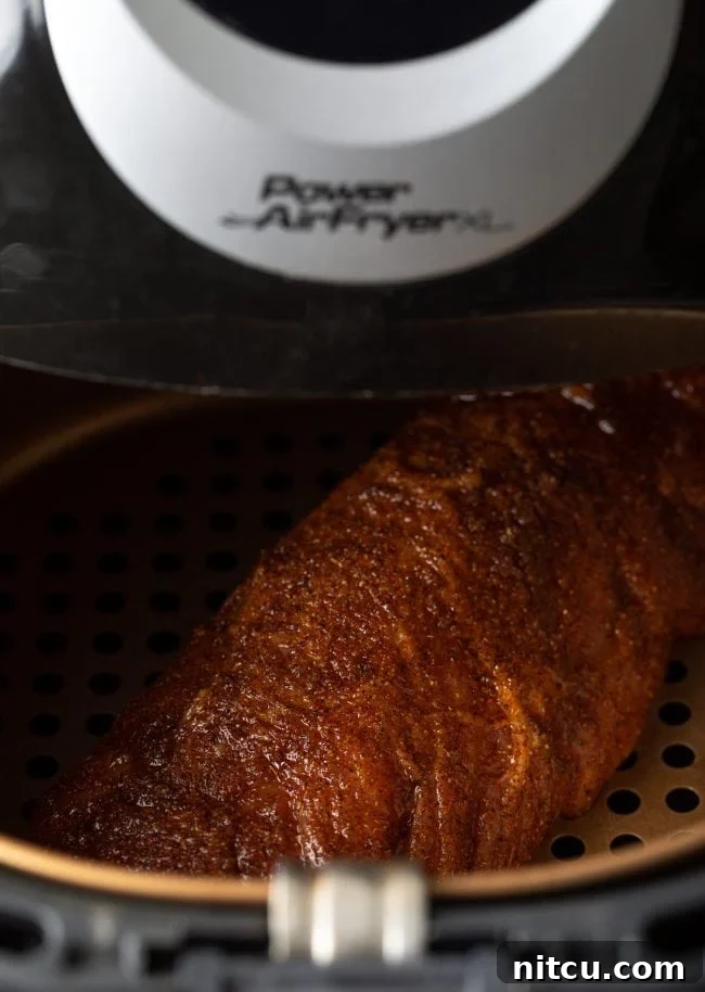 A spice-crusted pork loin cooking inside an air fryer basket, with its exterior already starting to brown.