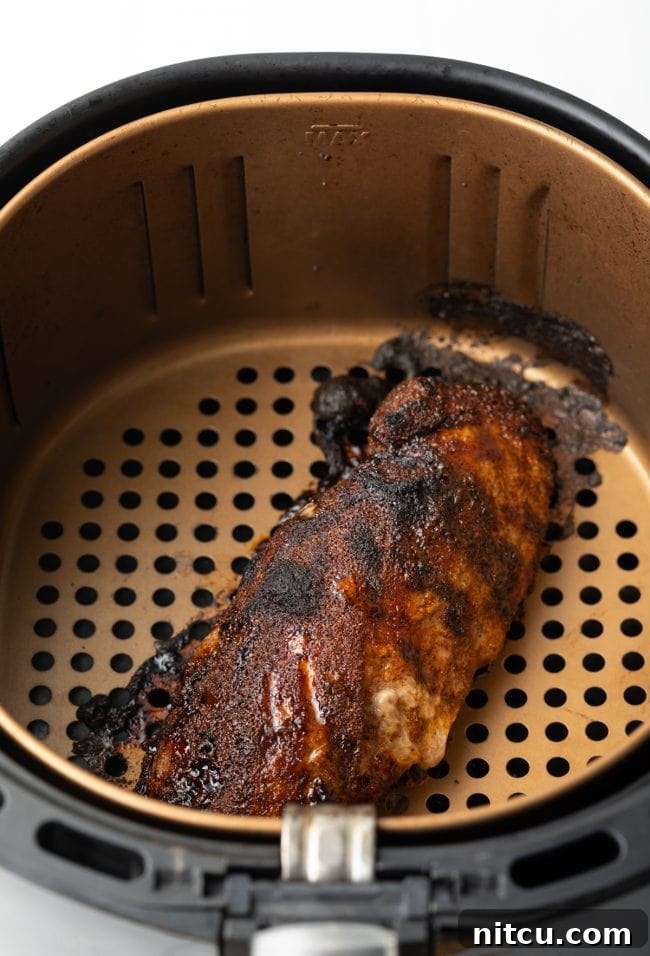 A perfectly cooked pork loin with a dark, flavorful crust, still in the air fryer basket after cooking.