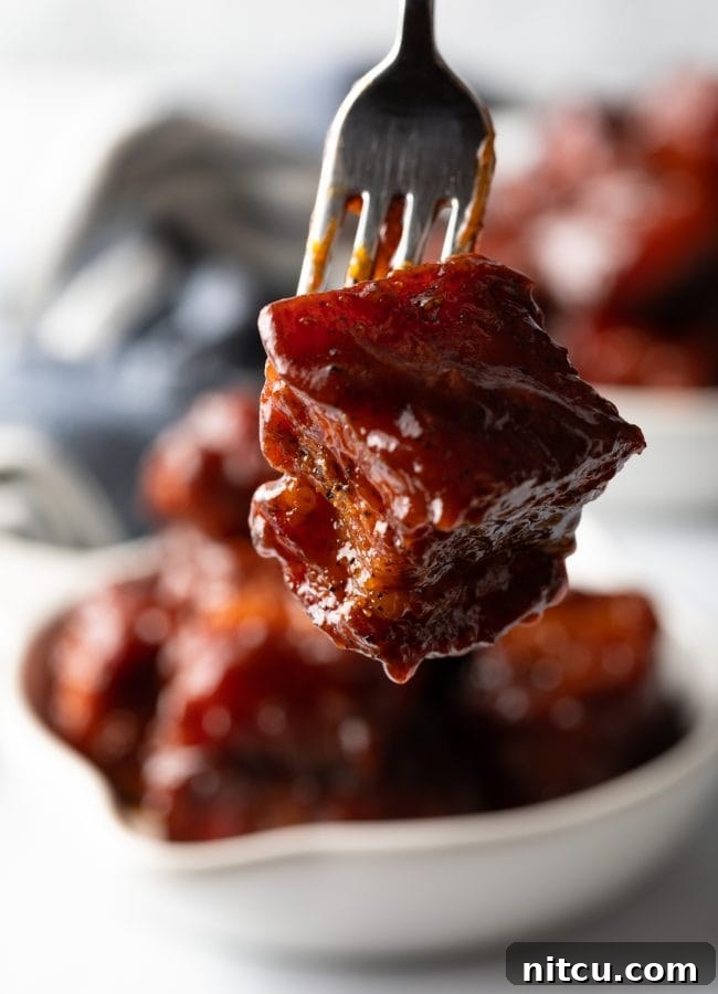 BBQ Pork Belly Candy Bites 5 A fork holding a perfectly glazed cube of smoked pork belly burnt ends, ready to be eaten.