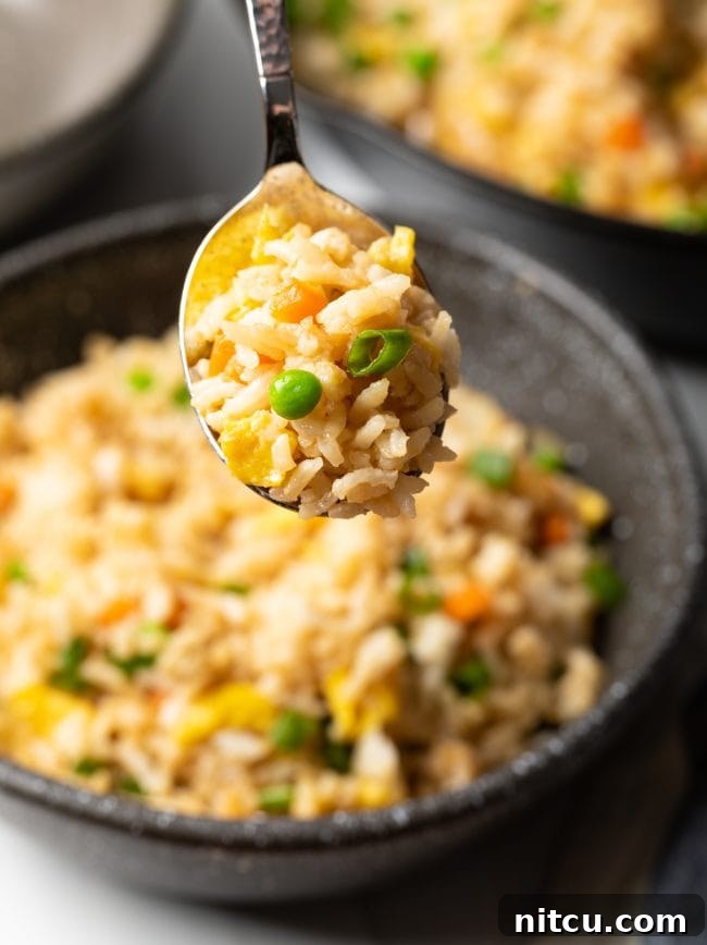 Perfect Homemade Hibachi Rice 4 Spoonful of hibachi rice with eggs and veggies held towards camera, showcasing its texture.