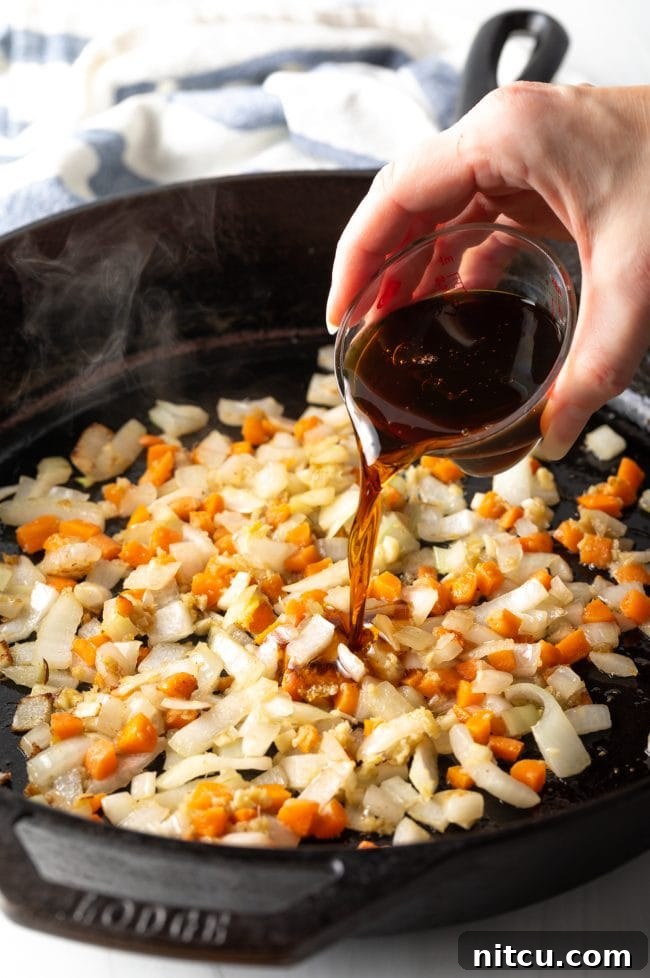 Perfect Homemade Hibachi Rice 10 A hand pouring savory sauces over sautéed vegetables, creating a rich aroma.