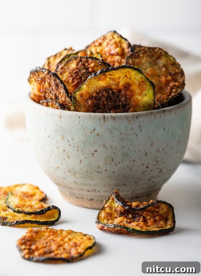 Crispy Air-Fried Zucchini Bites 11 A speckled bowl overflowing with fried zucchini chips, with several chips playfully scattered around the bowl on a wooden surface.