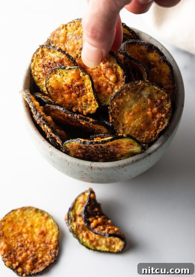 Crispy Air-Fried Zucchini Bites 4 Top down view of a hand reaching into a bowl filled with golden-brown air-fried zucchini chips.