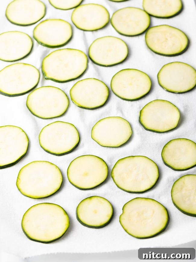 Crispy Air-Fried Zucchini Bites 7 Raw, thinly sliced zucchini laid out in a single layer on a paper towel, ready for patting dry.