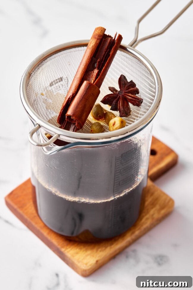 Finest Chai Tea Blends 6 Straining freshly brewed chai tea concentrate into a pitcher, separating the rich liquid from the infused spices and tea leaves.