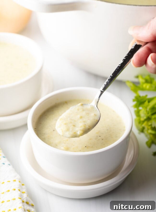 Bowl with cream of celery soup, hand holding spoon scooping up soup.