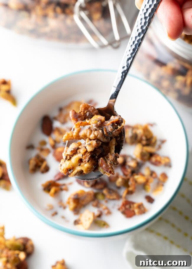 Ultimate Keto Granola 16 Top view of a spoon with granola and milk held towards the camera, above a bowl of granola.
