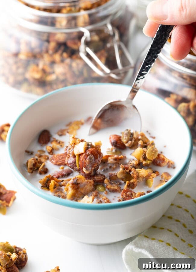 Ultimate Keto Granola 4 Bowl with keto granola and milk, with a hand scooping the granola with a spoon.