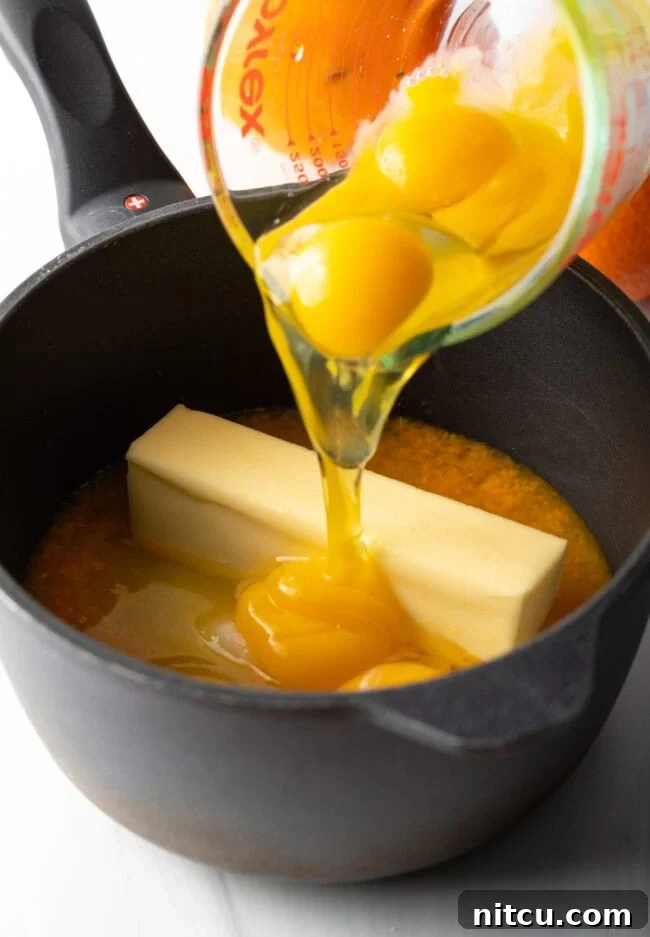 Sunshine Orange Curd 7 Glass measuring bowl adding egg yolks and butter to the pot. A glass measuring bowl being used to add egg yolks and cubes of butter into a saucepan. This step illustrates the careful incorporation of key ingredients that will give the orange curd its rich, creamy texture.