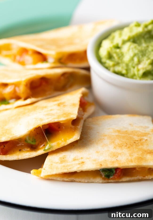 Effortless Shrimp Quesadilla Delight 2 Pieces of shrimp quesadilla on a plate, with a small bowl of guacamole.