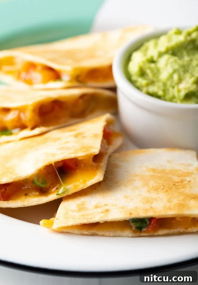 Effortless Shrimp Quesadilla Delight 10 Closeup view of slices of shrimp quesadilla ontop of plate with guacamole filled ramekin in the background.