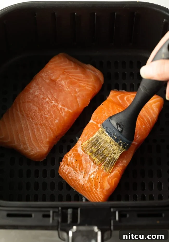 Crispy Skin Air Fryer Frozen Salmon 7 Hand brushing seasonings over uncooked salmon fillets in the air fryer.