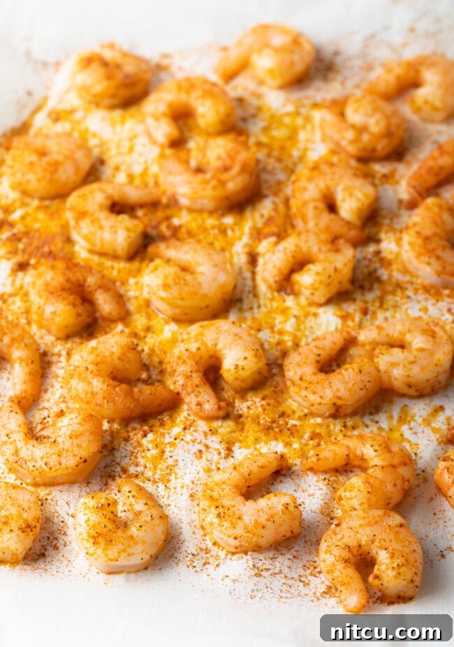 Cajun Shrimp Crostini 5 Oven-baked seasoned shrimp spread in a single layer on a parchment-lined baking sheet, showing their pink, curled shape.