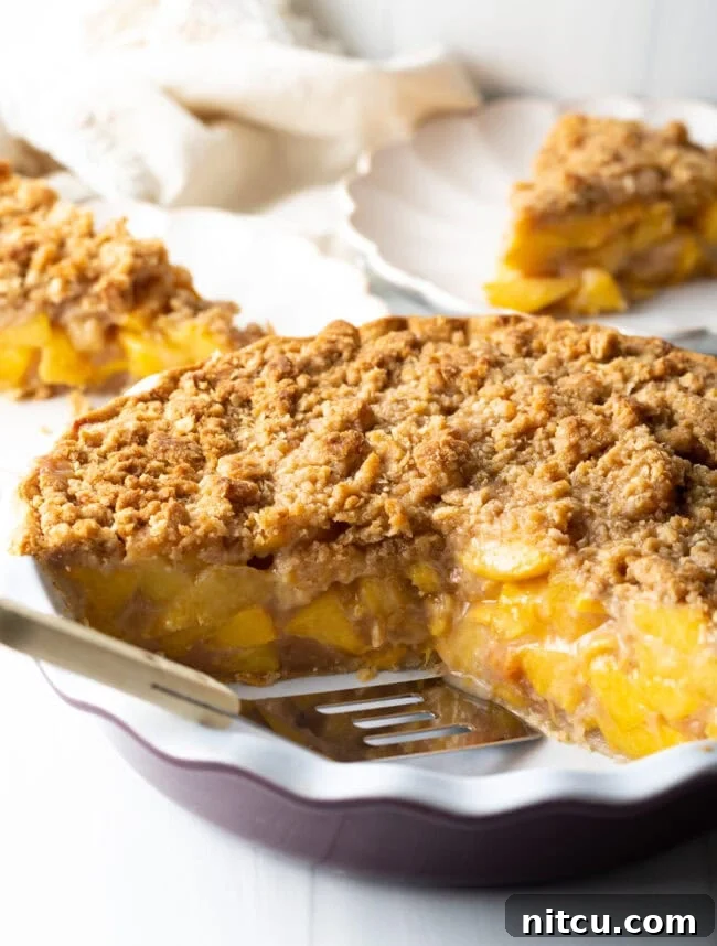 Anytime Peach Pie 2 A golden-brown peach crumble pie, freshly baked, with a spatula ready to serve a slice.