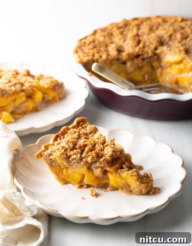 Anytime Peach Pie 4 A single slice of freshly baked peach crumble pie on a white plate, showcasing its golden crust and juicy peach filling.