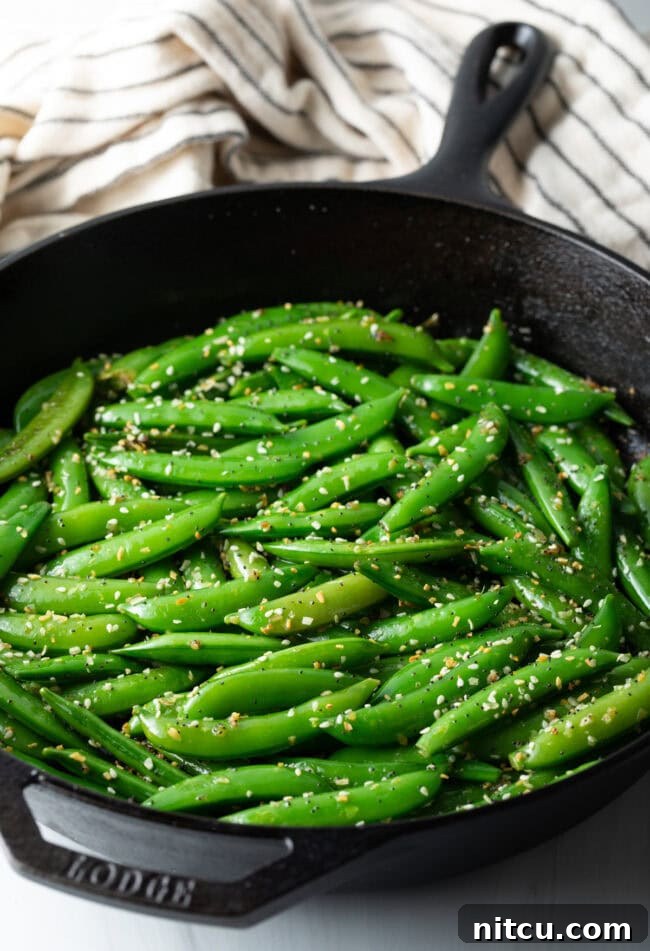 Crispy Garlic Snap Pea Stir Fry 2 Top down view of vibrant green sugar snap peas stir-frying in a skillet with sesame seeds.
