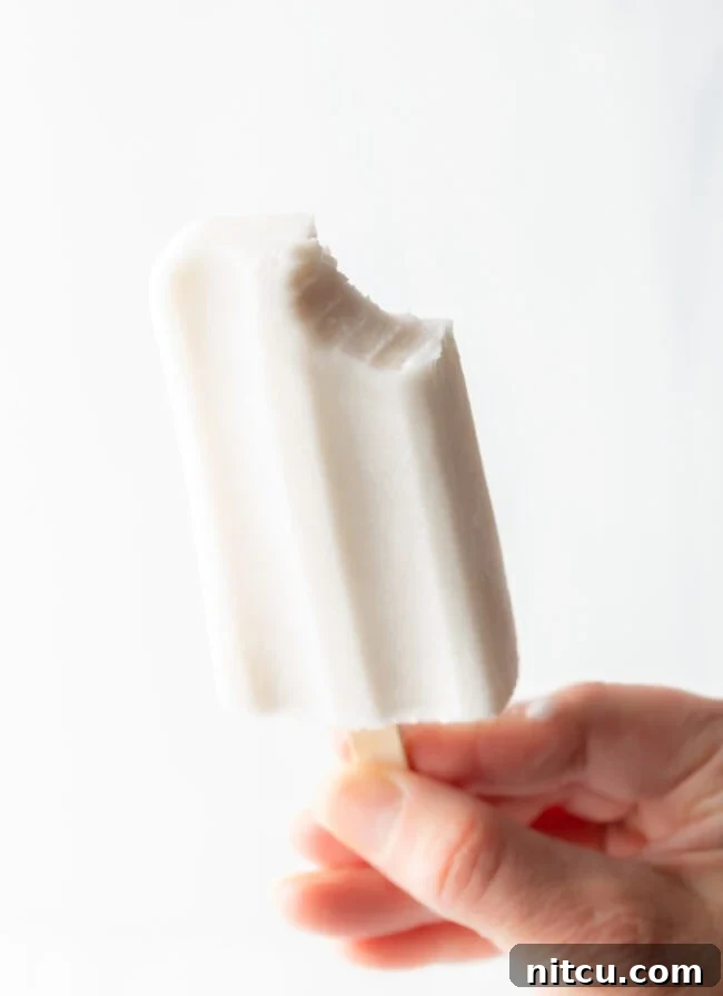 Creamy Dairy-Free Coconut Popsicles 3 A hand holding a perfectly creamy coconut milk popsicle with a small bite taken out, highlighting its smooth texture.