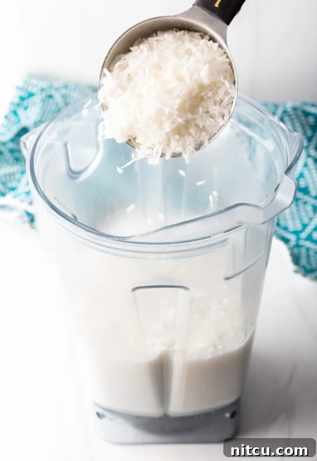 Creamy Dairy-Free Coconut Popsicles 5 Shredded coconut being added to a blender with creamy coconut milk, sugar, vanilla, and salt for the popsicle mixture.