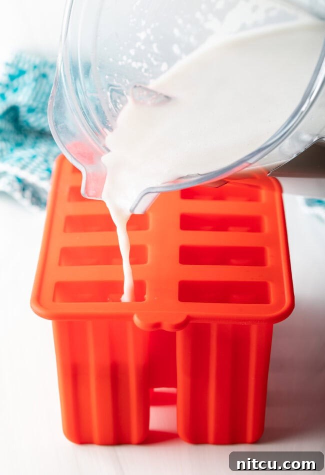 Creamy Dairy-Free Coconut Popsicles 6 The creamy coconut milk mixture being poured into individual compartments of a popsicle mold.