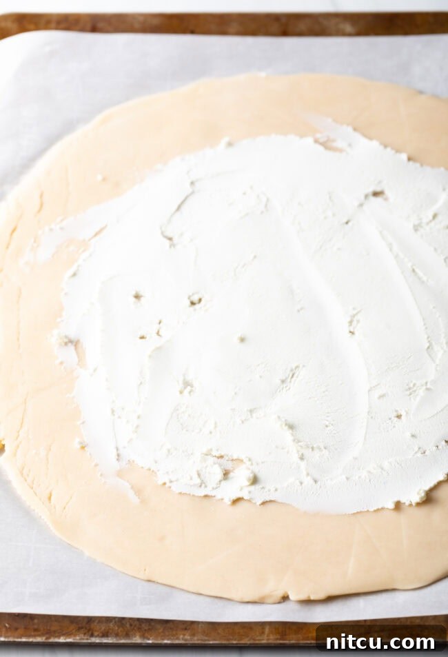 Rustic Italian Tomato Pie 7 Step-by-step image of softened goat cheese being spread evenly over the pie crust, leaving a rim.