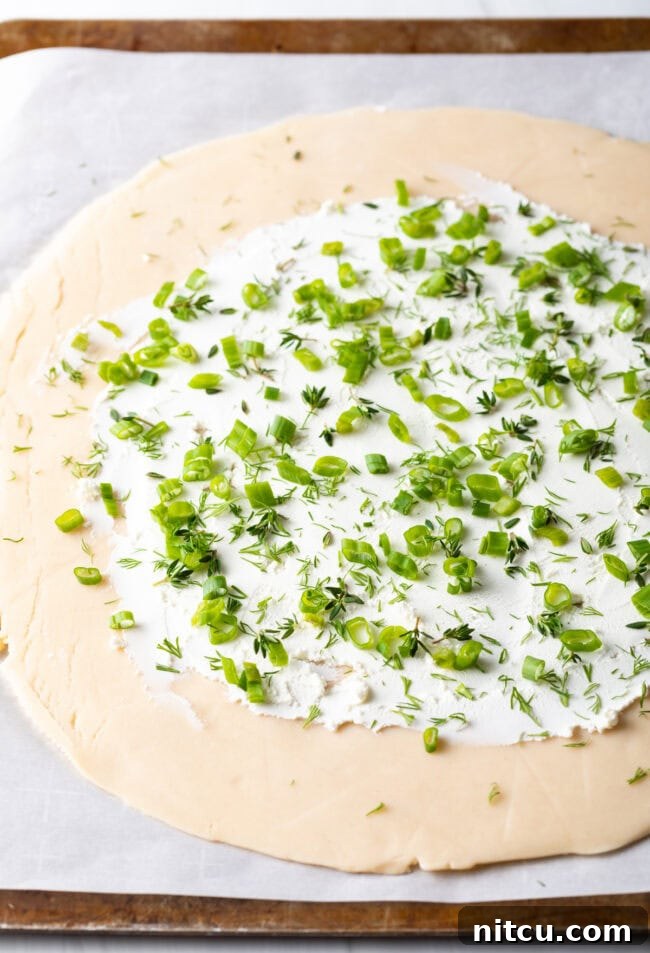Rustic Italian Tomato Pie 8 Step-by-step image of chopped scallions, thyme, and dill sprinkled over the goat cheese layer.
