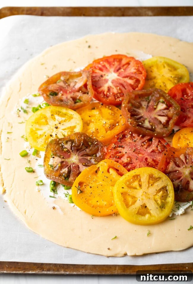 Rustic Italian Tomato Pie 9 Step-by-step image of sliced heirloom tomatoes being carefully arranged and overlapped on top of the herb and goat cheese layer.