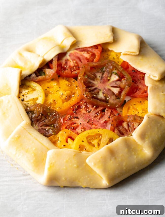 Rustic Italian Tomato Pie 10 Step-by-step image showing the edge of the pie crust being folded over the tomatoes to create a rustic crimped border.