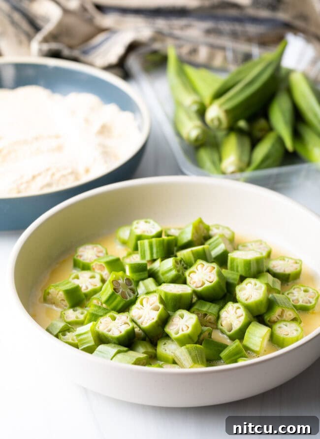 Crispy Air Fryer Okra Fries 8 Raw pieces of okra in egg wash bowl.