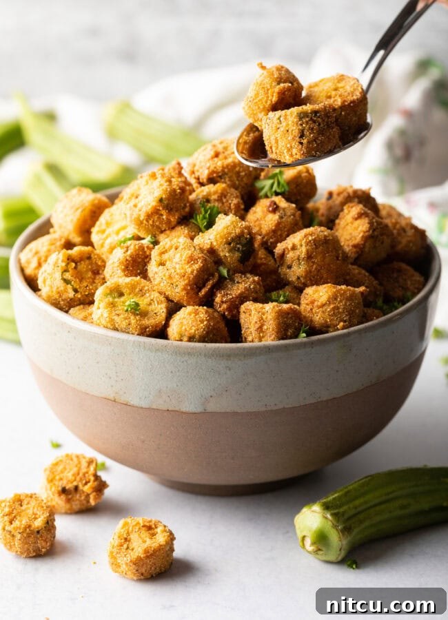 Southern Fried Okra Bliss 11 A spoon carefully adding golden pieces of Southern fried okra into a serving bowl.