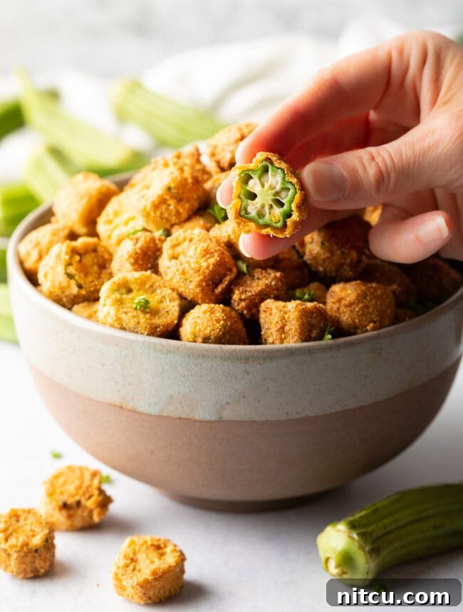 Southern Fried Okra Bliss 12 A hand holding a perfectly sliced and breaded piece of fried okra up to the camera, showcasing its golden exterior.