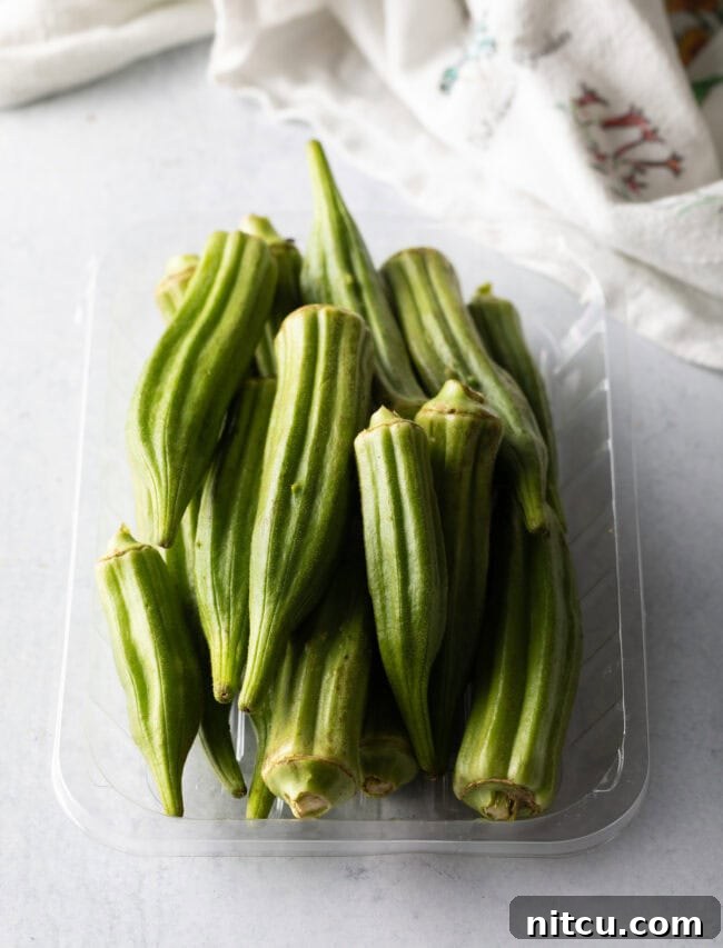 Southern Fried Okra Bliss 4 Raw, whole okra pods displayed in a clear plastic container, showing their fresh, vibrant green color and readiness for preparation.