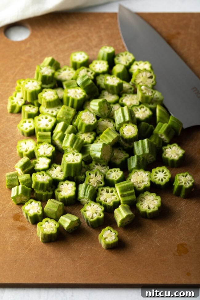 Southern Fried Okra Bliss 6 Fresh okra being sliced into uniform rounds on a wooden cutting board with a chef's knife.