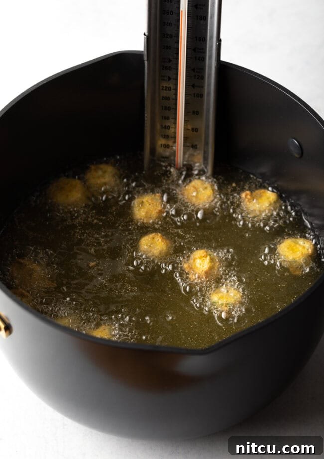 Southern Fried Okra Bliss 10 Breaded okra pieces sizzling and frying in hot oil within a large pot, turning golden brown.