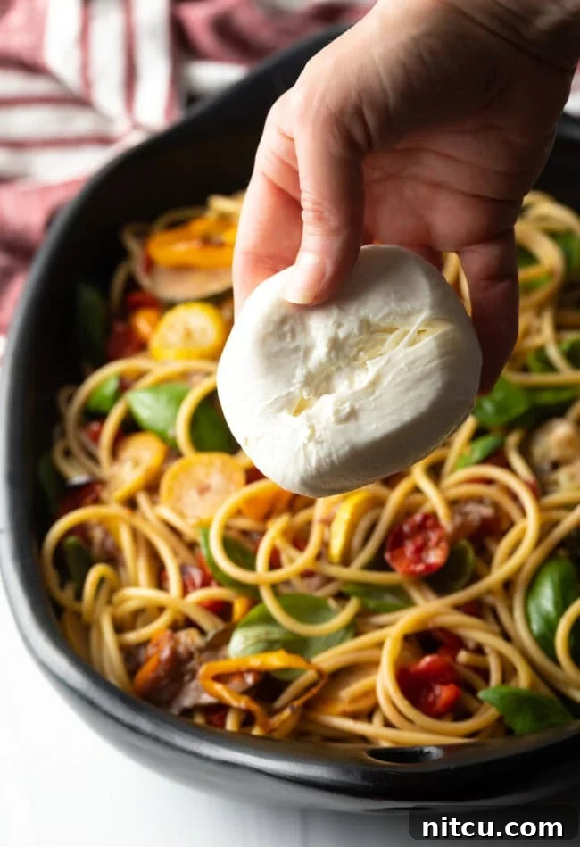 Creamy Burrata and Roasted Summer Harvest Pasta 13 Hand adding a ball of burrata cheese, split in half, to the finished pasta dish.