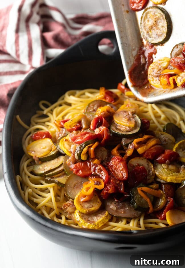 Creamy Burrata and Roasted Summer Harvest Pasta 10 Pouring roasted vegetables and sauce over the spaghetti in a large bowl.