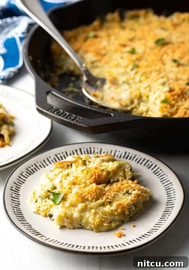 Golden Zucchini Gratin 2 Plate with zucchini casserole serving on it. Cast iron with casserole in background.