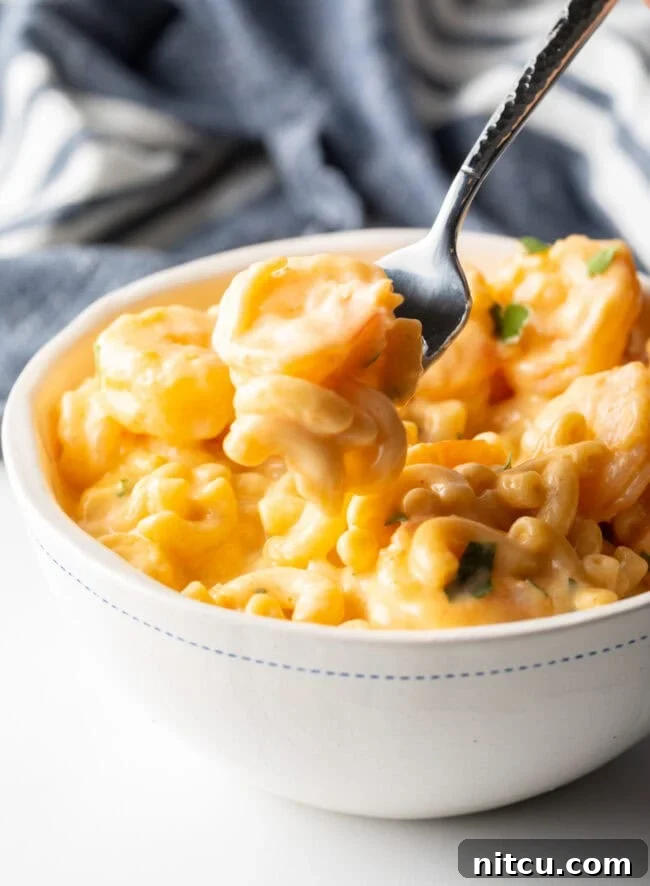 Decadent Shrimp Macaroni and Cheese 12 Bowl with a generous serving of shrimp mac & cheese, a fork taking a bite from the bowl, showing the creamy texture.