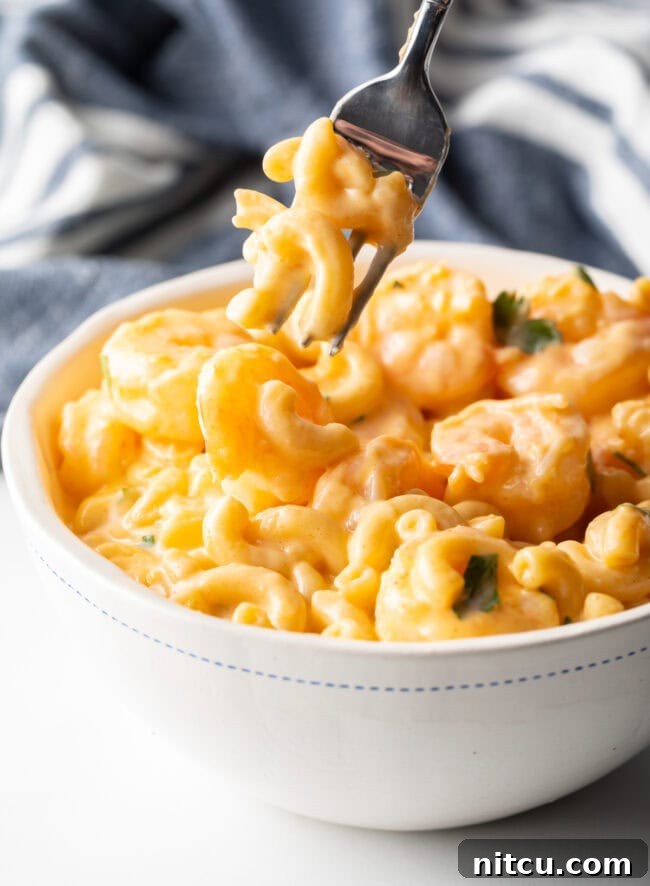 Decadent Shrimp Macaroni and Cheese 5 Fork taking a generous bite of creamy macaroni with cheese and shrimp from a bowl.