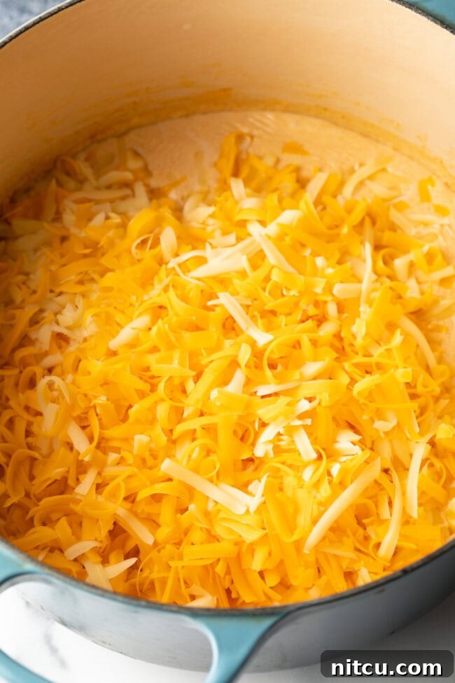 Decadent Shrimp Macaroni and Cheese 7 Freshly shredded cheese being added to the pot with the creamy sauce base.