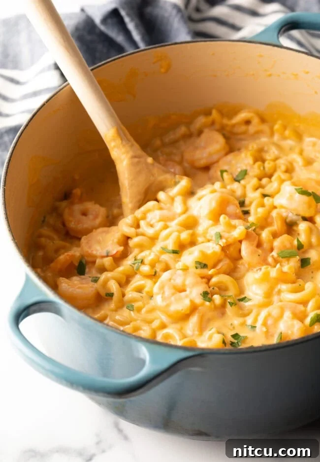 Decadent Shrimp Macaroni and Cheese 10 Top down view of a cooking pot with a wooden spoon and the finished, creamy shrimp mac and cheese dish.