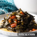 A small mound of Jamaican collard greens on a white plate, garnished with a red pepper slice.