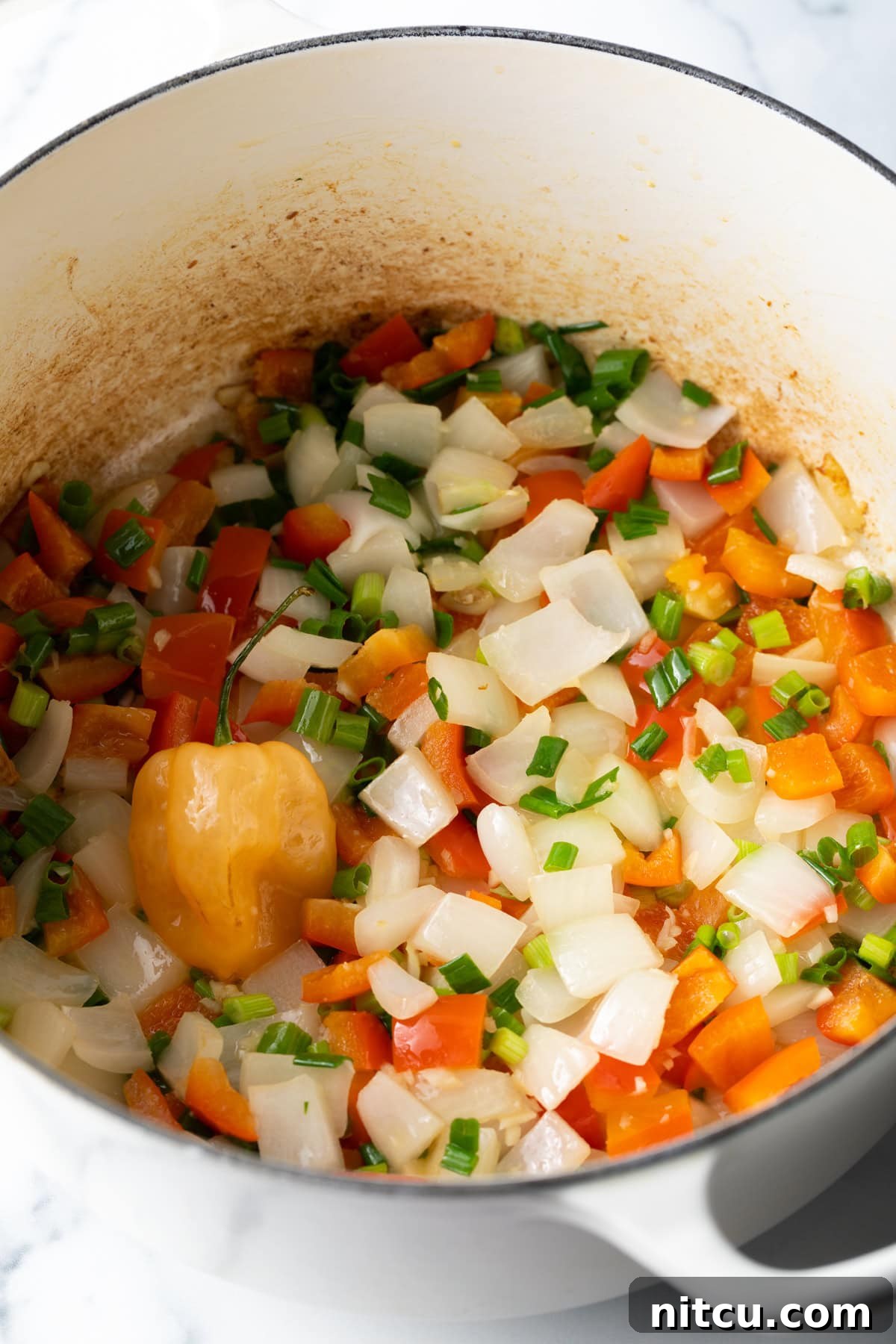 Vibrant Caribbean Callaloo 5 Chopped onions, red bell peppers and veggies sauteeing in a pot. A close-up shot of chopped onions, red bell peppers, and other vibrant vegetables gently sautéing in a large pot, forming the aromatic base of the dish.