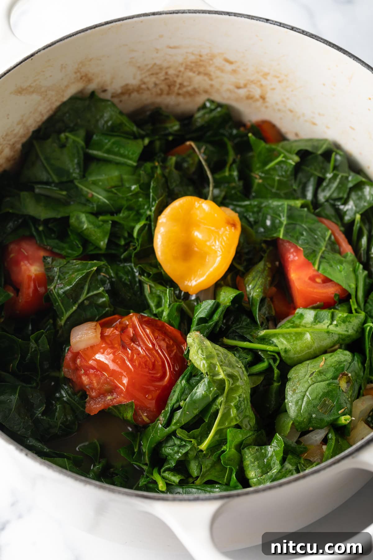 Vibrant Caribbean Callaloo 6 Pot loaded up with collard greens and tomato wedges. A large pot generously filled with fresh collard greens and vibrant tomato wedges, ready for simmering.